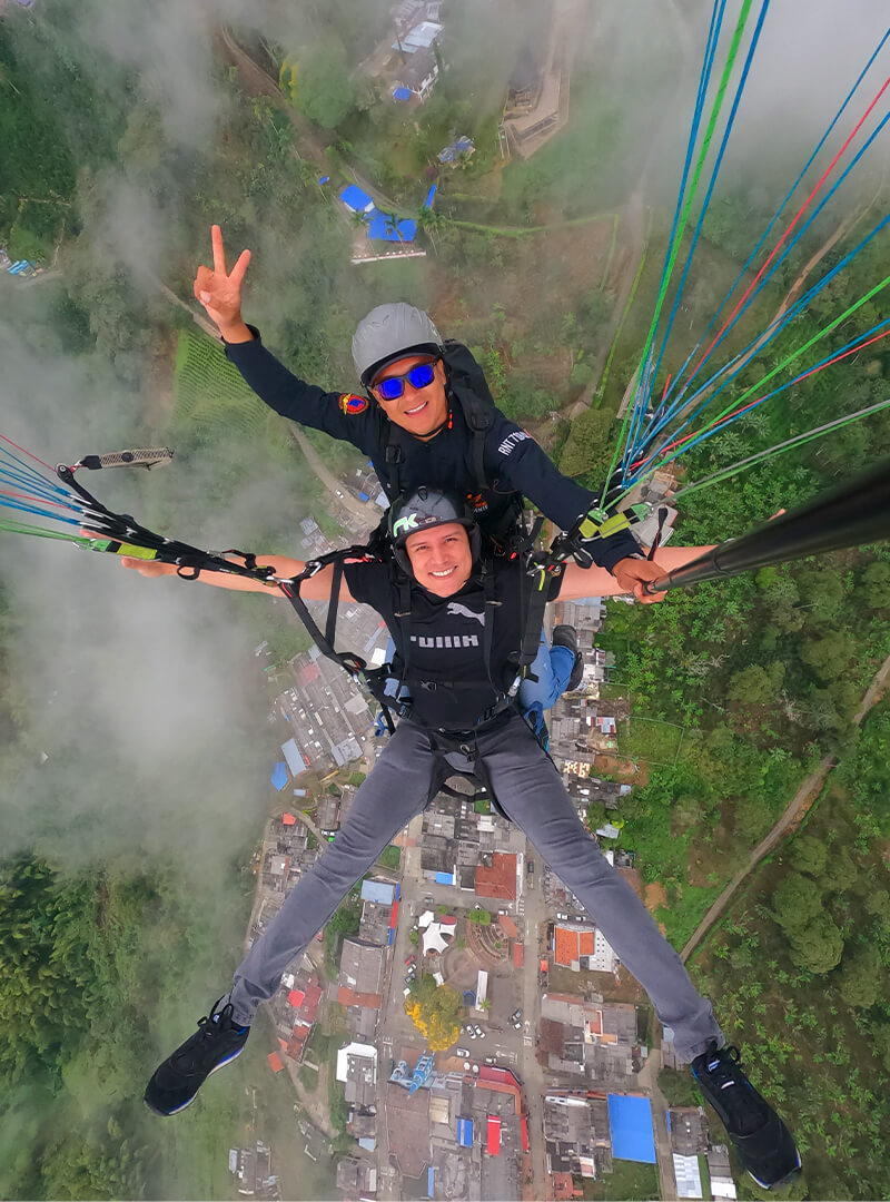 Pasajero y piloto volando en parapente sobre paisaje verde